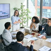 Senior female ceo and multicultural business people discussing company presentation at boardroom table. Diverse corporate team working together in modern meeting room office. Top view through glass