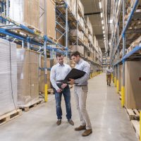 Two men with folder talking in factory warehouse