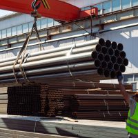 Worker transporting stack of metal pipes with gantry crane in the steel factory
